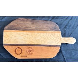 A paddle-shaped serving board made of maple, walnut, and cherry wood with a handle, displayed on a blue background.