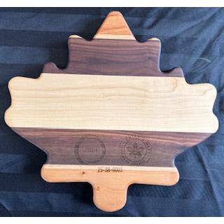 A maple leaf shaped serving board with varying shades of wood, including areas that appear to be walnut and cherry wood, with the text 'Essex County' engraved in the center.
